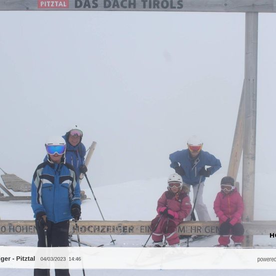 Eine Gruppe von Menschen skifahren auf einem verschneiten Hang. Sie tragen Helme, Schutzbrillen und Skianzüge. Das Holzschild zeigt PITZTAL DAS DACH TIROLS. Das Foto hat einen Wasserzeichen mit dem Text HOCHER PITTAL 04/03/2023 14:46.