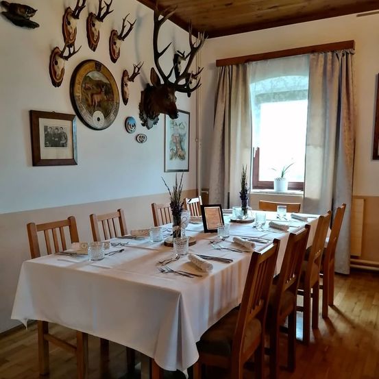 Ein Esszimmer für eine Mahlzeit vorbereitet mit einem langen Tisch, der in Weiß bedeckt ist, umgeben von Holzstühlen, und dekoriert mit Hirschköpfen und gerahmten Bildern an der Wand.