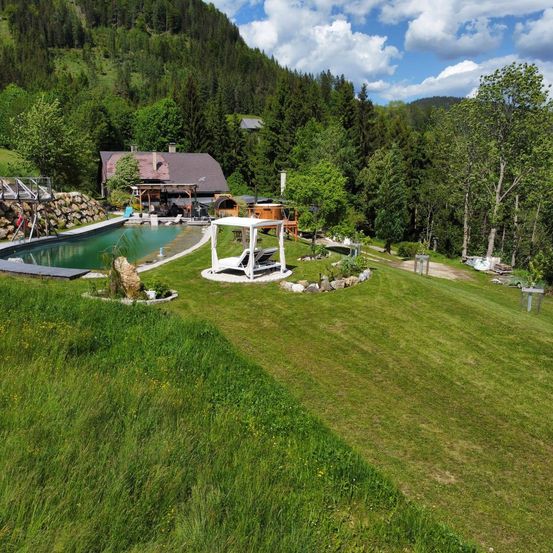 Luftaufnahme eines Hauses mit Swimmingpool und Pavillon vor dem Hintergrund üppiger grüner Hügel.