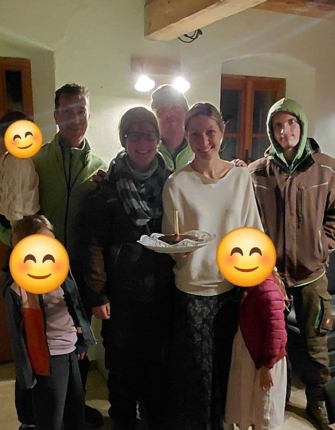 Ein Familienfoto mit lächelnden Gesichtern im Hintergrund. Eine Frau hält einen Teller mit Essen und einer Kerze.