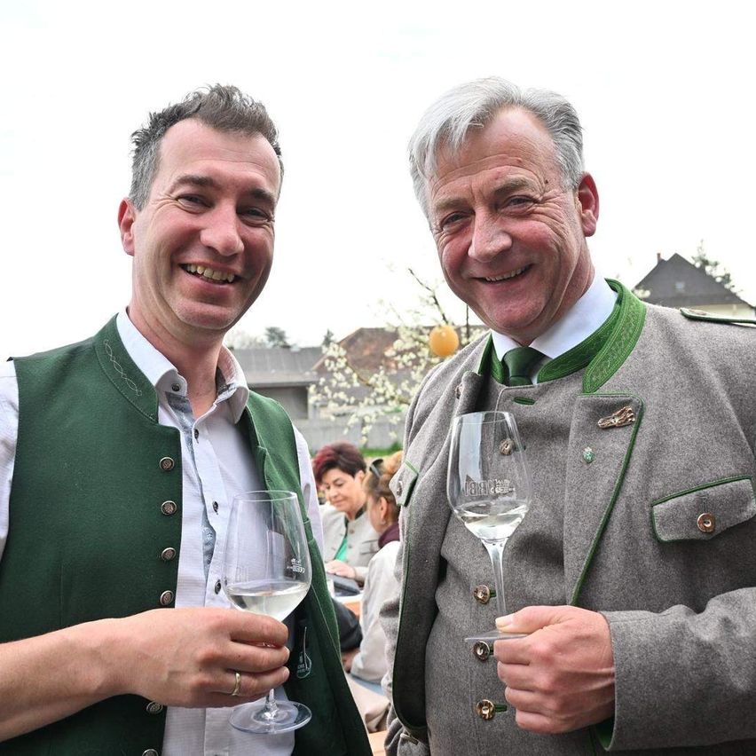Zwei Männer lächeln und halten Weingläser bei einer Veranstaltung im Freien, möglicherweise ein Bierfestival.