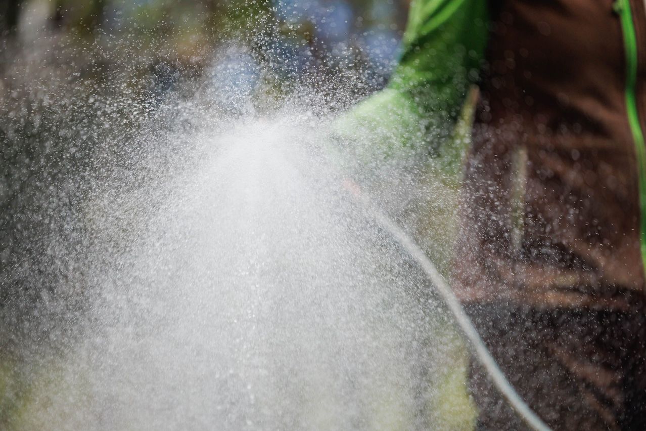 A person sprays water into the air, creating a misty effect. The water droplets scatter in various directions.