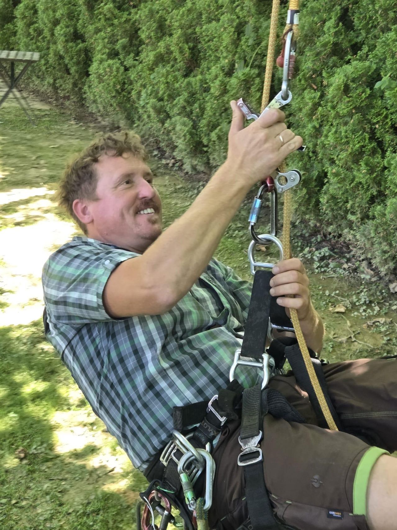 Bergsteiger mit Seil und Klettergurt in einem Garten.