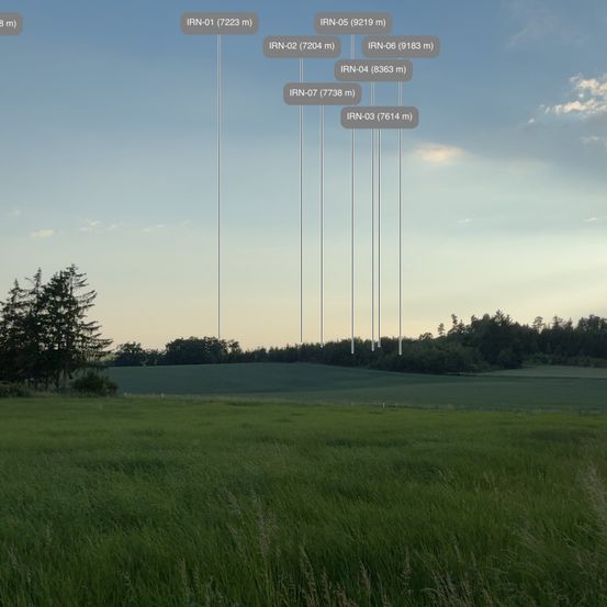 Eine weite, offene Wiese unter blauem Himmel mit verstreuten Bäumen, mit Beschriftungen, die Höhen in Metern angeben.