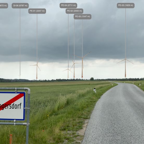 Das Bild zeigt eine Landschaft mit einer Straße, mehreren Windturbinen mit Höhenangaben und einem Schild mit der Aufschrift 'angersdorf'. Der Himmel ist bewölkt.
