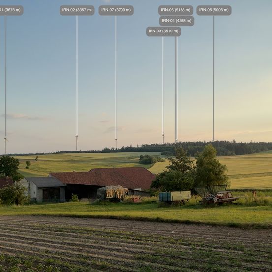 Ein Bauernhof mit mehreren Windturbinen im Hintergrund. Der Boden ist für die Bepflanzung vorbereitet.