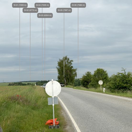 Eine Autobahn mit einem Schild am Straßenrand, zwei Autos in der Ferne und Bäumen auf beiden Seiten. Der Himmel ist bewölkt.