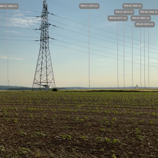 Landwirtschaftliches Feld mit einem Turm und Windturbinen im Hintergrund, mit verschiedenen Höhen in Metern beschriftet.