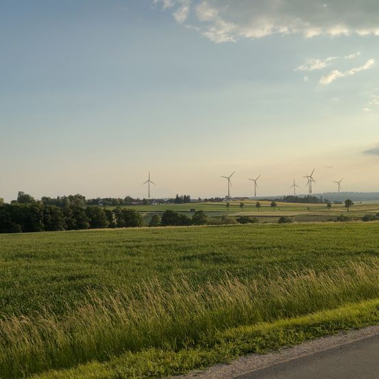 Eine Landschaft mit mehreren Windrädern in der Ferne und einem breiten Feld mit grünem Gras unter einem teilweise bewölkten Himmel.