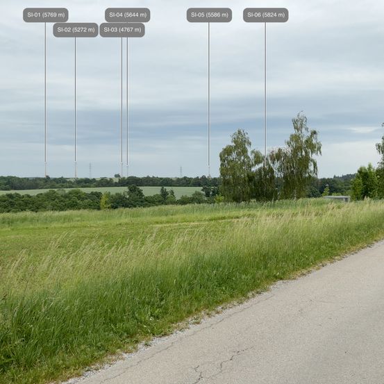 Eine weite ländliche Landschaft mit einem Grasfeld und einer Straßenrandansicht, gekennzeichnet durch mehrere Entfernungen zu Sendetürmen.