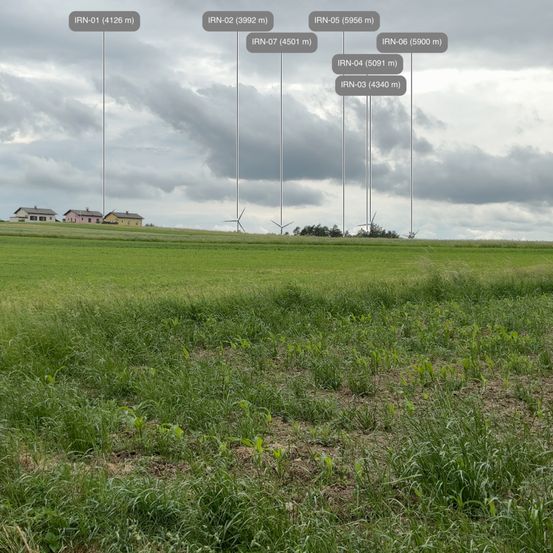 Eine Luftaufnahme eines grasigen Feldes mit mehreren hohen Masten, die mit Codes und Höhen gekennzeichnet sind. Der Himmel ist bewölkt.