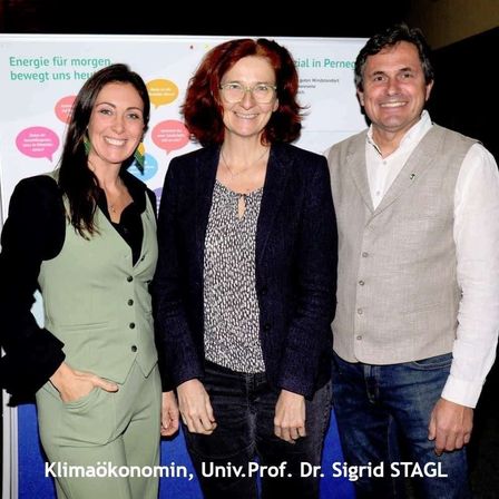 Drei Personen stehen nebeneinander vor einem Schild. Zwei Frauen und ein Mann lächeln und posieren für ein Foto. Das Schild hat den Text 'Energie für morgen bewegt uns heu'.