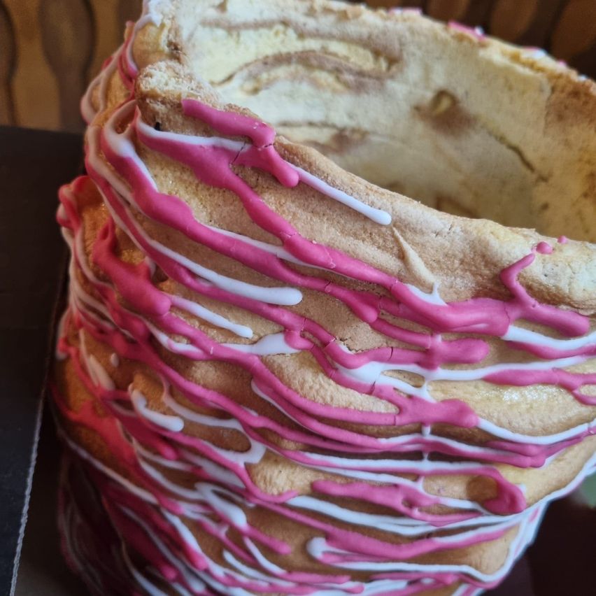 Eine Nahaufnahme eines Kuchens, der mit rosa und weißer Glasur spiralförmig gestaltet ist und einem verwirbelten Dessert ähnelt, möglicherweise ein erdbeergeschmackiger Biskuitkuchen mit vertikal gestapelten Schichten.
