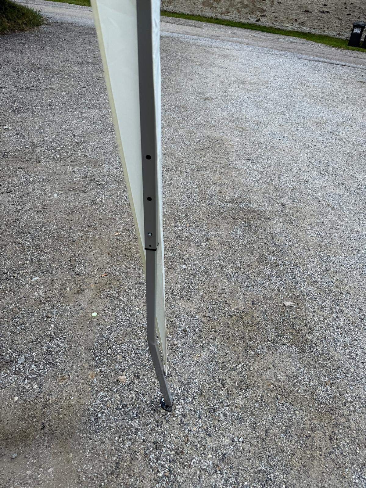 Ein Metallpfosten steht auf Kies mit einem weißen Stoff befestigt, gesichert durch Metallschrauben.