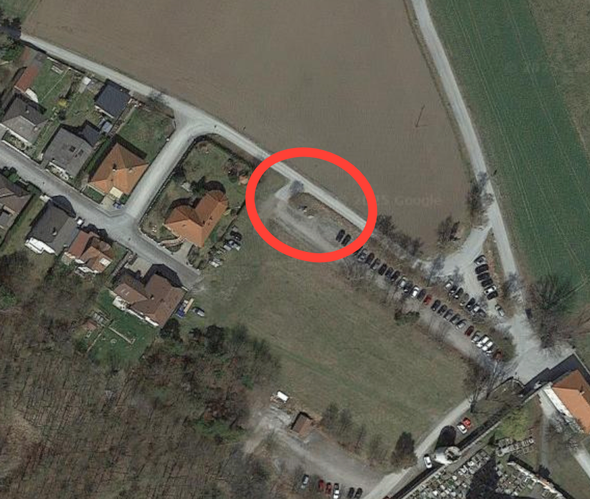 Luftaufnahme eines ländlichen Gebiets mit mehreren Häusern und einem rot markierten Bereich. Rechts ist ein Friedhof zu sehen.