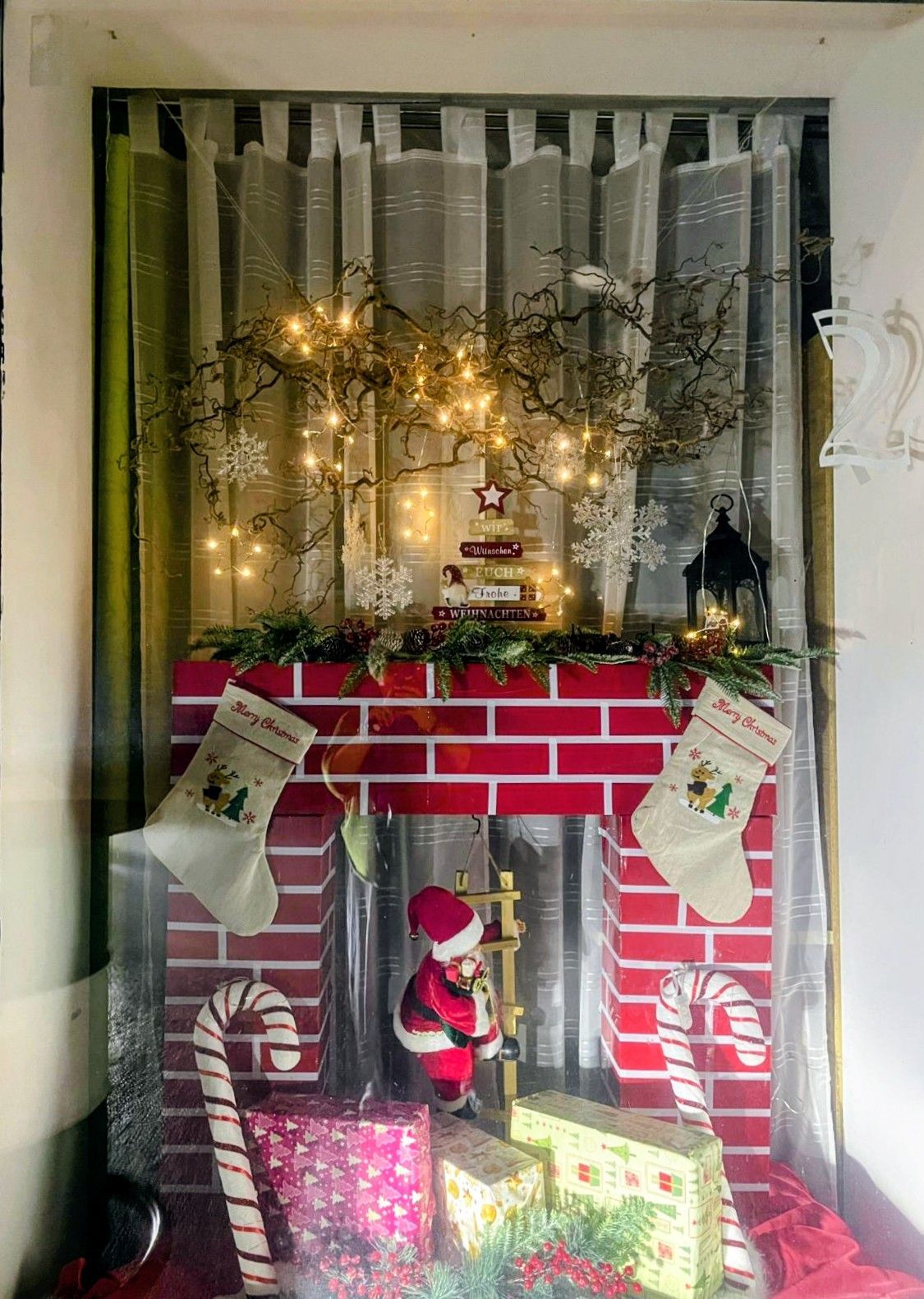 Eine festliche Weihnachtsdekoration mit einem roten Backsteinkamin, Strümpfen, einer Santa-Figur und einer Girlande mit Lichtern und Schneeflocken.