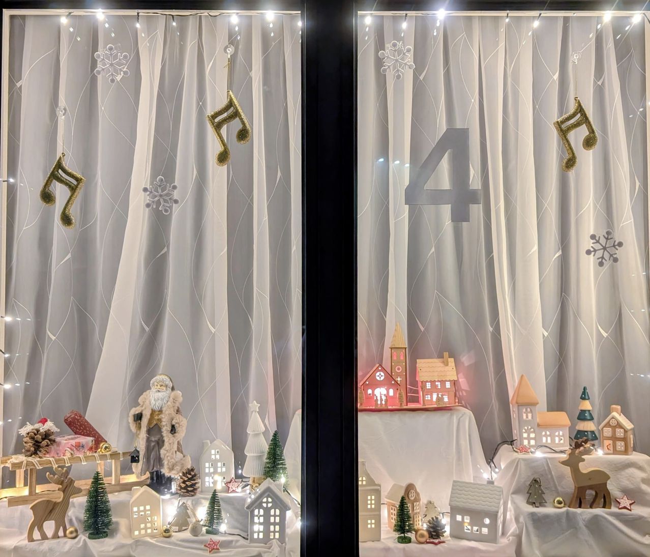 Eine Weihnachtsdekoration mit einer Weihnachtsmannfigur, einem Schlitten und verschiedenen Häusern. Die Szene ist mit Lichtern beleuchtet und mit Schneeflocken und Musiknoten dekoriert.