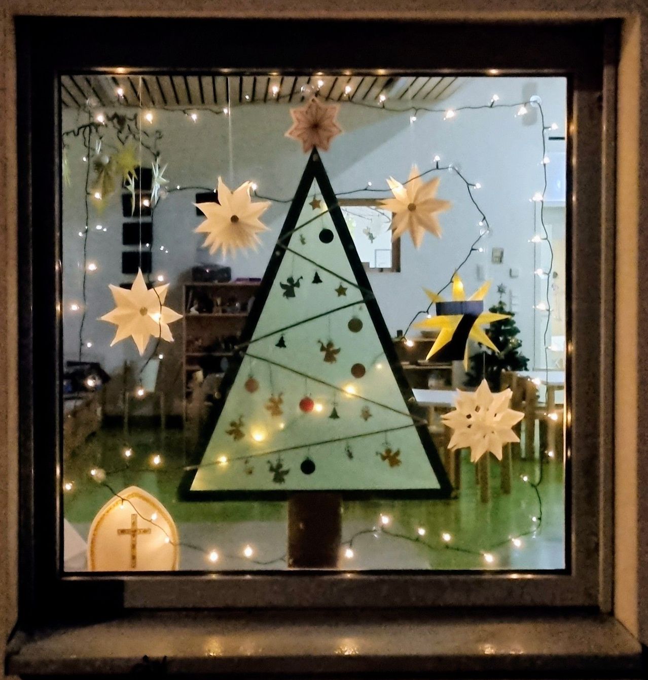 A framed window displays a festive Christmas tree with paper snowflakes and lights, reflecting a room with a green floor.