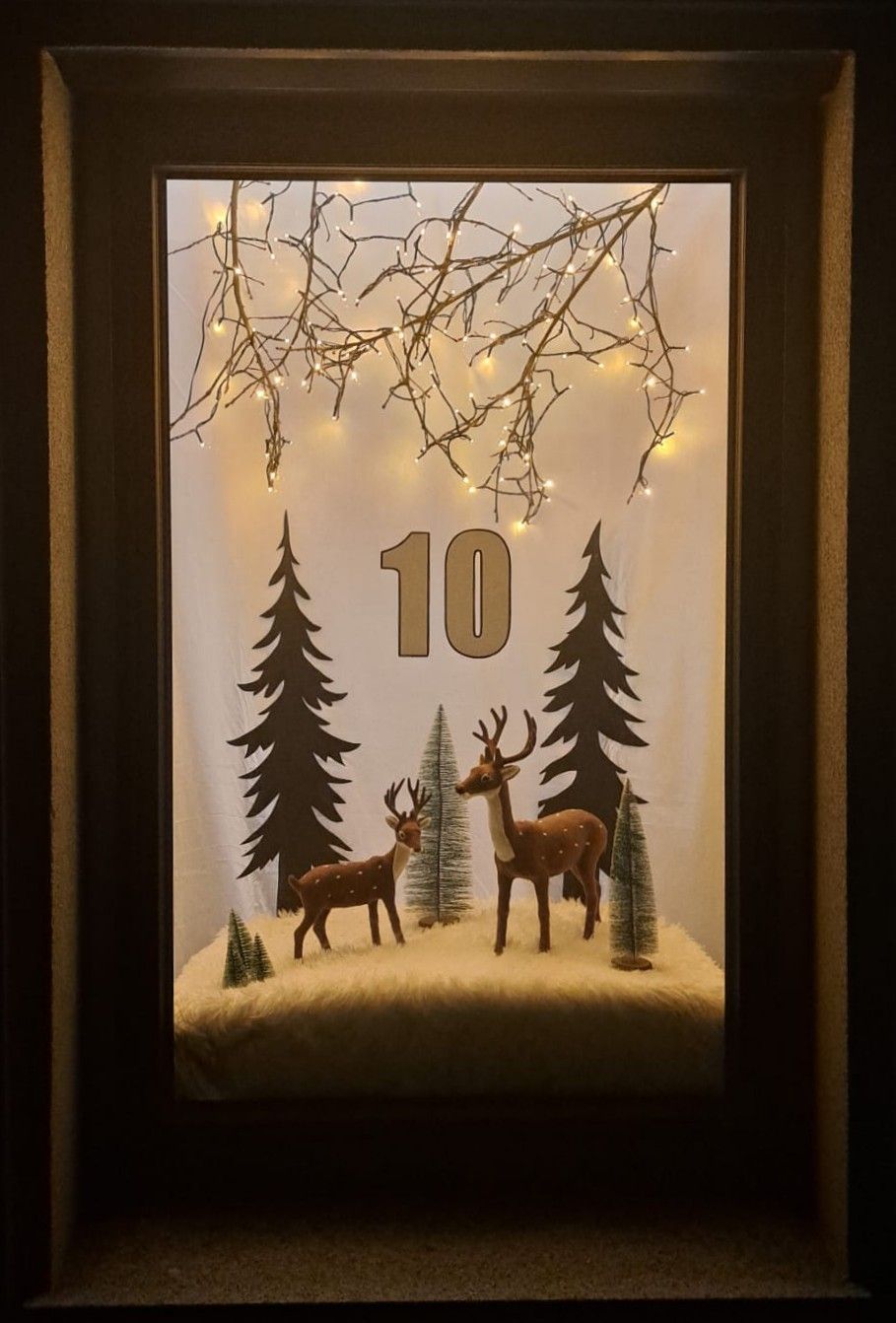 Ein gerahmte Winterszene zeigt zwei Rehe, Bäume und die Nummer 10, mit einem Zweig von Feelichtern darüber.