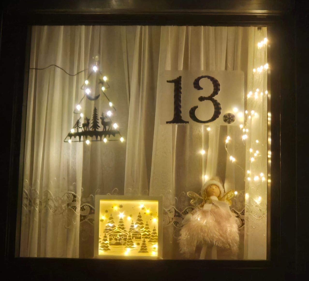 Ein Weihnachtsfenster-Display mit einem beleuchteten Weihnachtsbaum, einer Puppe und einem Schild mit der Nummer 13.