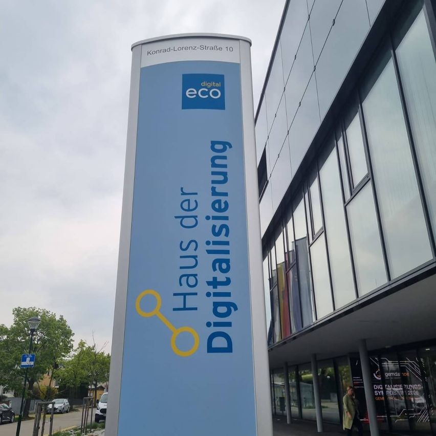Ein blaues Schild an einem Gebäude, das 'digital eco' und 'Digitalisierung' mit einem gelben Symbol auf der linken Seite zeigt.