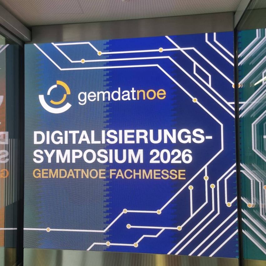 Ein blaues digitales Plakat mit einem Schaltkreis-Design zeigt 'Digitalisierungs-Symposium 2026' und 'GEMDATNOE Fachmesse'. Das Plakat hat ein gelbes und weißes Logo auf der linken Seite.