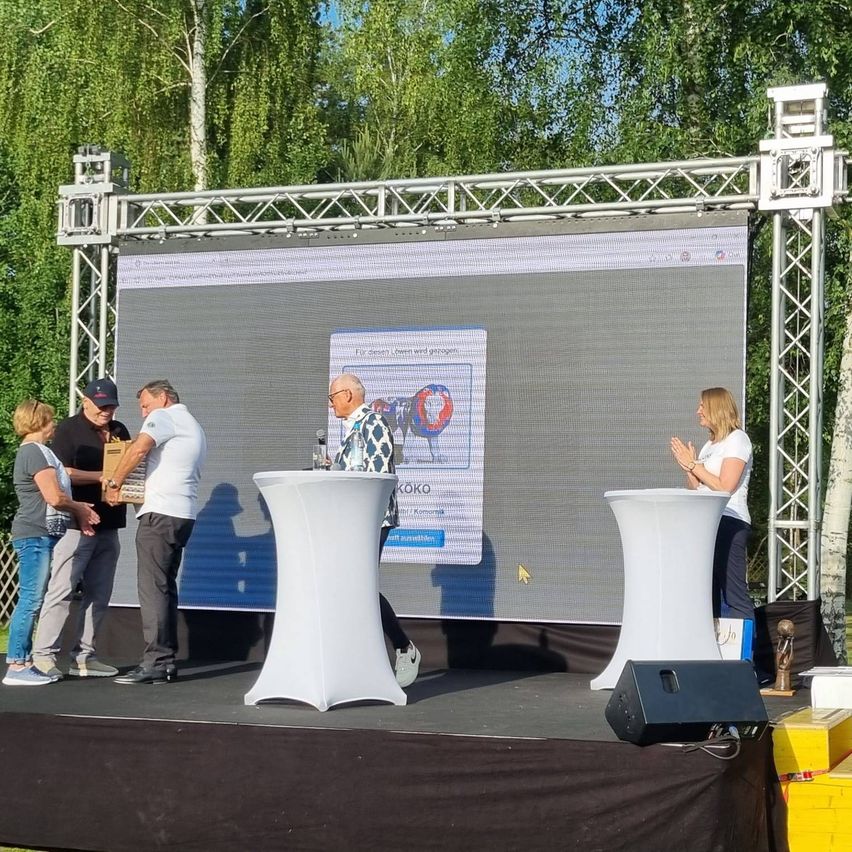 Five people stand on a stage in front of a large screen showing an image of a cow. One man holds a box.