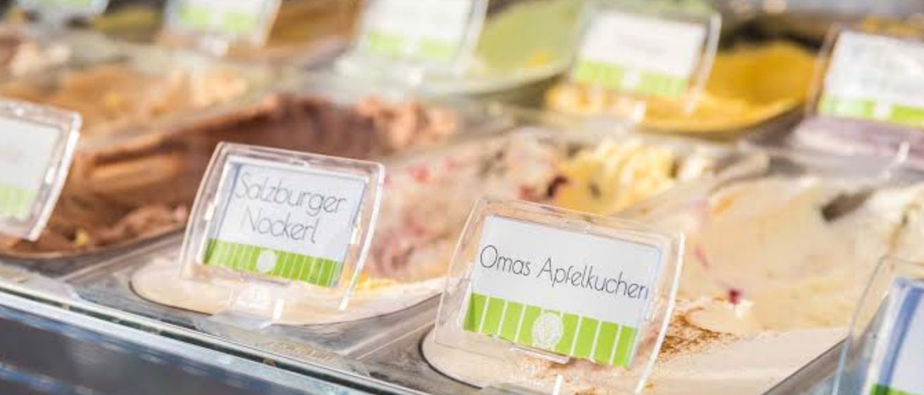 Eine Vitrine mit mehreren Desserts. Es gibt zwei beschriftete Schalen: Salzburger Nockerl und Omas Apfelkuchen. Die Desserts sind in verschiedenen Geschmacksrichtungen.