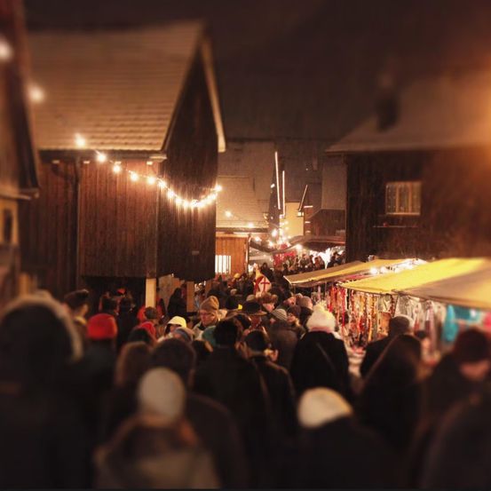 A busy street market at night with many people, tents, and lights. Some people are wearing hats and scarves.