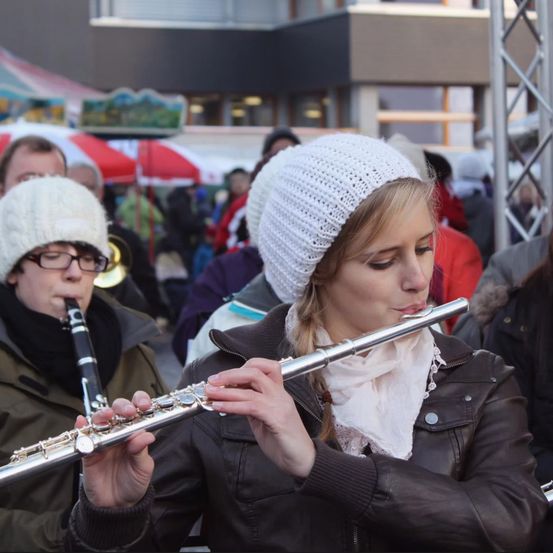 A woman plays the flute while another woman plays the clarinet in a crowd of people during a winter festival.