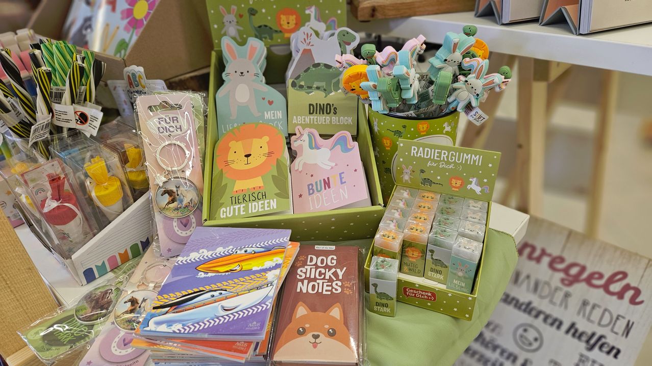Eine Ausstellung von Kinderprodukten, einschließlich Bücher, Aufkleber und Spielzeug, auf einem grünen Tisch. Die Produkte zeigen Tiere, Dinosaurier und andere farbenfrohe Designs.