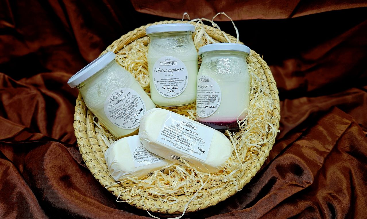 A wicker basket contains three jars of yogurt and two blocks of butter, all labeled with a white sticker on a brown background.