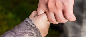 Ein Nahaufnahme einer Erwachsenenhand, die die Hand eines Kindes hält, mit einem unscharfen grünen Hintergrund.