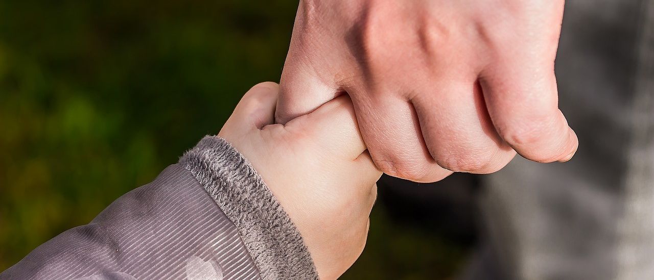 Ein Nahaufnahme einer Erwachsenenhand, die die Hand eines Kindes hält, mit einem unscharfen grünen Hintergrund.