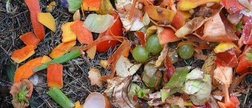 Ein hölzerner Kompostbehälter gefüllt mit verschiedenen organischen Abfällen wie Bananenschalen, Zwiebelstücken und anderen Gemüseresten.