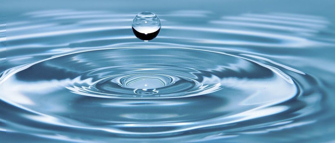 Ein Wassertropfen in der Luft kurz bevor er in einen Wasserkörper fällt und Wellen erzeugt.