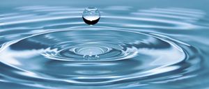 Ein Wassertropfen in der Luft kurz bevor er in einen Wasserkörper fällt und Wellen erzeugt.