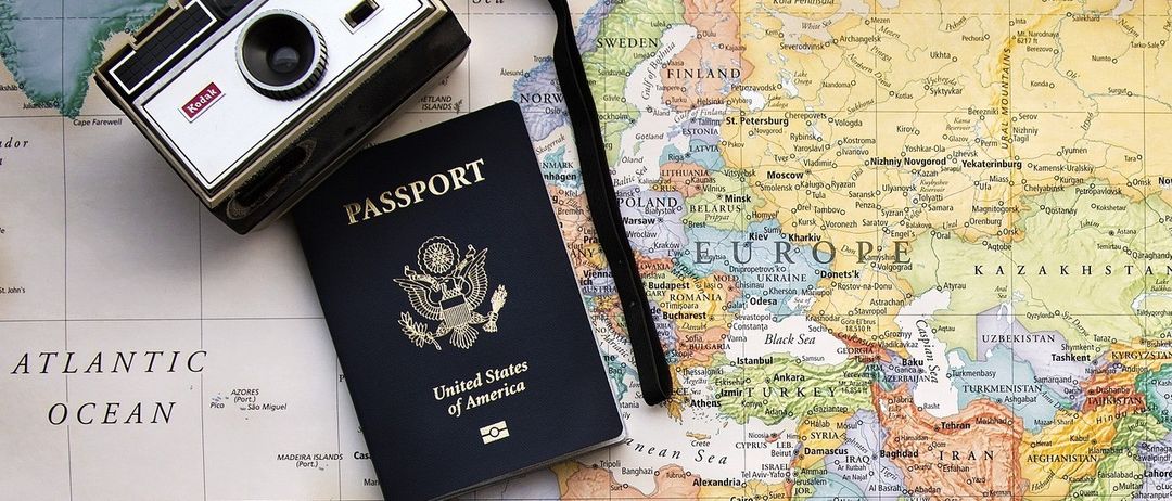 Ein US-Pass und eine alte Kamera liegen auf einer Weltkarte, wobei Europa, Asien und Afrika deutlich sichtbar sind.