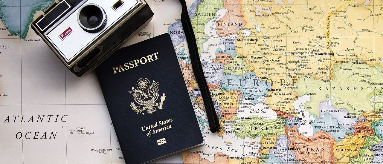 Ein US-Pass und eine alte Kamera liegen auf einer Weltkarte, wobei Europa, Asien und Afrika deutlich sichtbar sind.