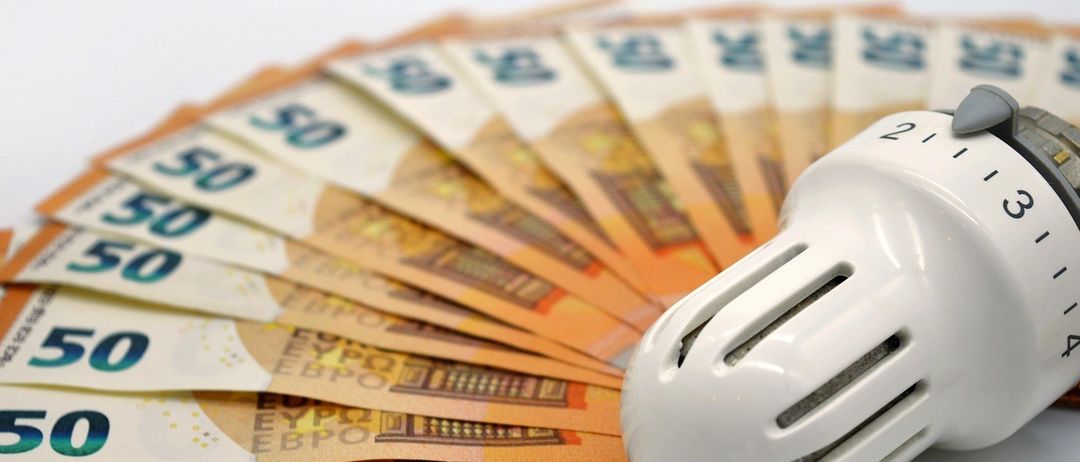 Eine Nahaufnahme eines Ventilators neben einem Stapel Euro-Banknoten. Die Banknoten sind ausgefächert, und der Ventilator hat eine weiße, zylindrische Form.