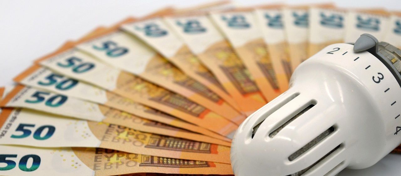 Eine Nahaufnahme eines Ventilators neben einem Stapel Euro-Banknoten. Die Banknoten sind ausgefächert, und der Ventilator hat eine weiße, zylindrische Form.