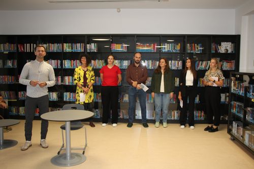 Eine Gruppe von Menschen steht in einer Bibliothek. Sie alle schauen nach vorne.