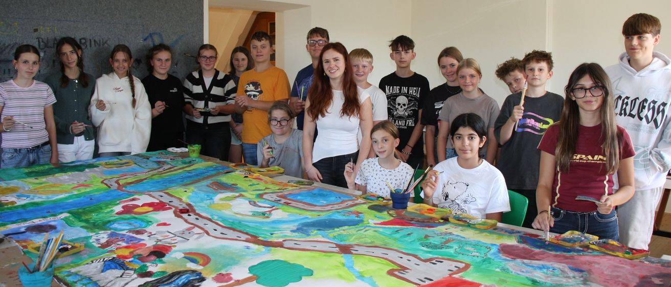 Eine Gruppe junger Menschen versammelt sich um einen großen Tisch und arbeitet an einem farbenfrohen Gemälde.