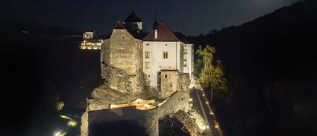 Eine mittelalterliche Burg auf einem felsigen Felsen ist bei Nacht beleuchtet, mit einem hellen Mond darüber. Die Burg hat Steinmauern und Türme und einen Weg, der zu ihr führt.