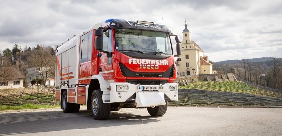 Ein roter und weißer Feuerwehrwagen mit der Aufschrift 'Feuerwehr' vorne, geparkt vor einem Gebäude.