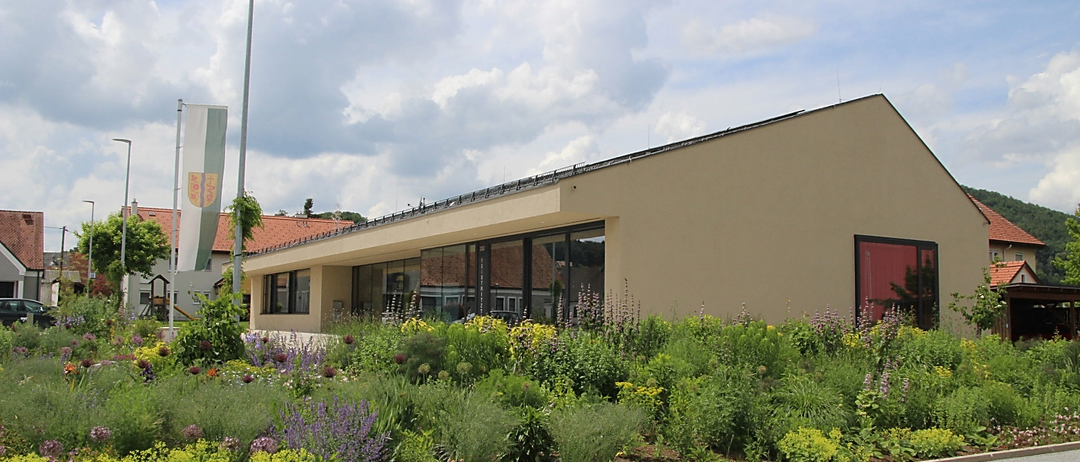 Ein Gebäude mit Glasfenstern und Solarpanelen befindet sich in einem Garten mit verschiedenen Blumen und Pflanzen.