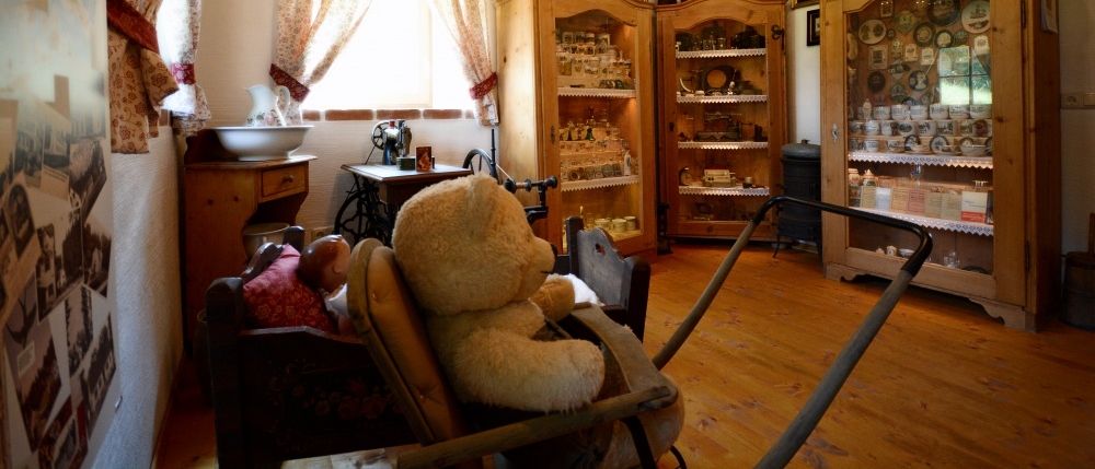 Ein gemütliches Zimmer mit Holzböden und Balken, ausgestattet mit einem Teddybären, einer Puppe und verschiedenen Holzschränken voller Gegenstände.