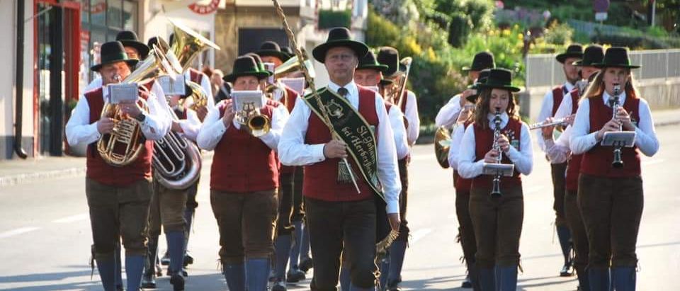 Eine Marschkapelle tritt im Freien auf. Sie sind in traditioneller Kleidung gekleidet und spielen verschiedene Musikinstrumente. Die Band geht in einer Parade die Straße entlang.