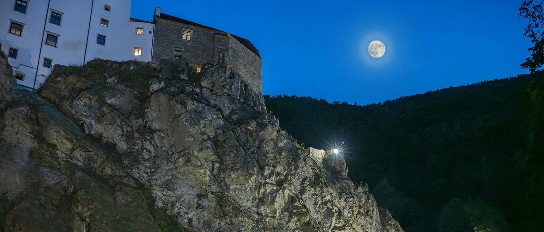 A castle perched on a cliff under a full moon at night, with a bright light on the cliff edge.