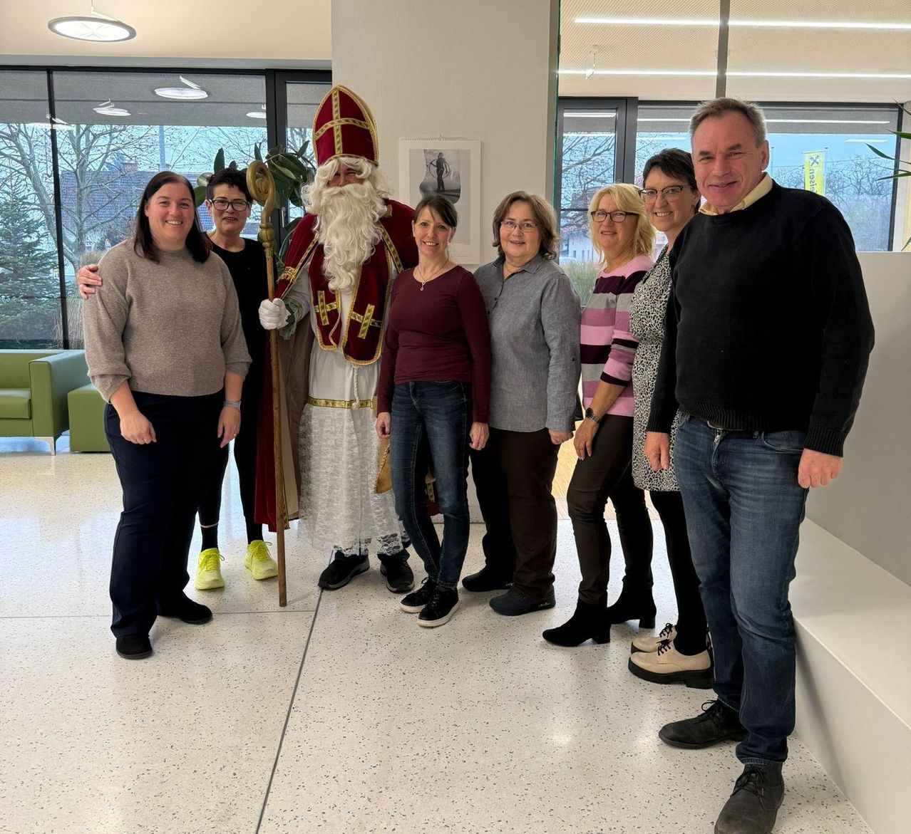A group of adults and a man dressed as Santa Claus are posing for a picture in a modern room.